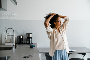 Black woman holding her hair while standing in kitchen at home