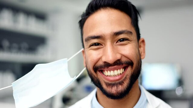 A happy researcher removing his face mask, finding a covid cure in a lab or end of a pandemic. Portrait of a smiling doctor or dentist. A medical professional with healthy teeth and good oral hygiene