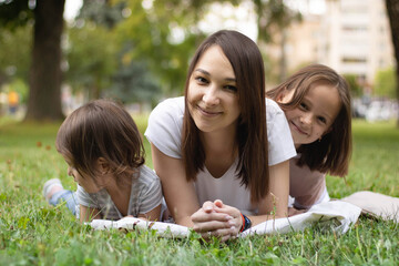 mother and daughters lie on the grass and each wants to attract attention