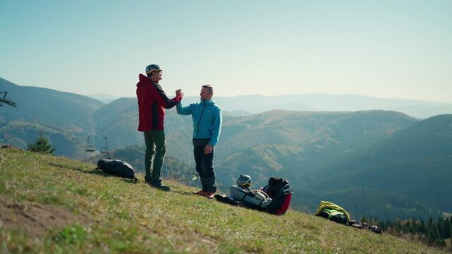 Paragliders high fiving after walking up hill to paragliding starting point, on a sunny morning in mountains.