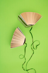 Old books and green ribbons on bright green background. Education, knowledge or nature concept. Flat lay. For book lovers.