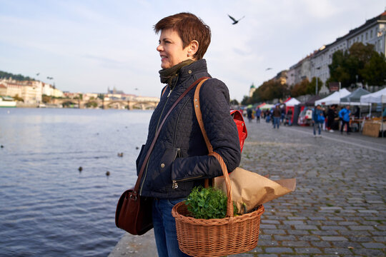 Woman at the Naplavka farmers market in Prague holding a wicker basket with vegetables and microgreens