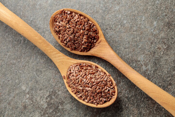 Wooden spoons with flaxseed on a stone background.