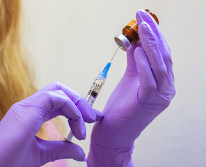 Young female doctor wearing purple rubber gloves holds an injection syringe in hands. Lip...