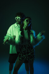 fashionable young models in sunglasses and trendy outfits posing on dark blue.