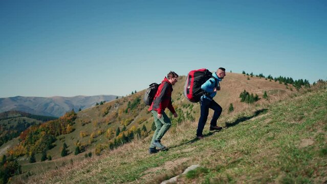 Paragliders, trekkers, mountaineers, walking up hill to a paragliding starting point, on a sunny morning in mountains.
