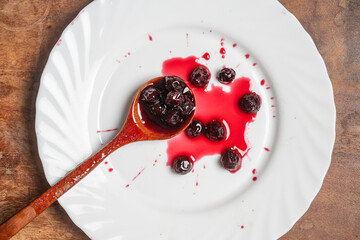 Red cherry jam in white plate with wooden spoon