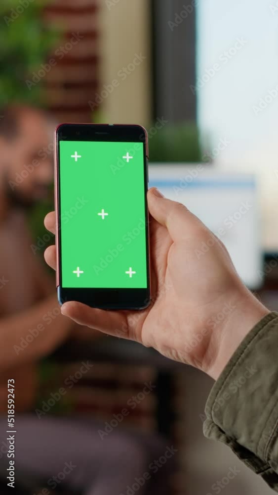 Poster vertical video: startup worker using isolated greenscreen on mobile phone, looking at blank mockup d