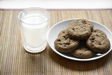 A glass glass with milk on a wooden mat with oatmeal cookies. Afternoon lunch with cookies. Sweet cookies with milk.