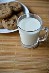 A glass glass with milk on a wooden mat with oatmeal cookies. Afternoon lunch with cookies. Sweet cookies with milk.