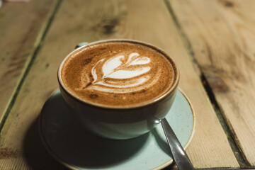 Cup with saucer and spoon on a wooden table. Coffee or cappuccino with leaf drawing