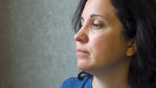 An adult woman sits against a wall. Oriental type of face. Dark hair. Thoughtful look. Indoors. Blogger. Forgiveness. Thoughts in my head. Sorrow and sadness. Close-up.