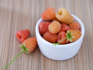 Yellow raspberries in white bowl with other yellow raspberries near them