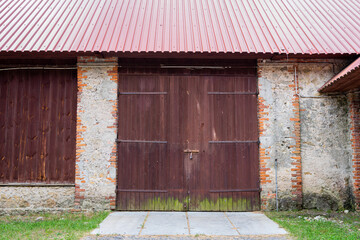 Fototapeta na wymiar The door to an old brick barn covered with a corrugated metal roof