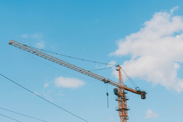 Yellow construction tower crane against blue sky.House under construction. Industrial skyline.