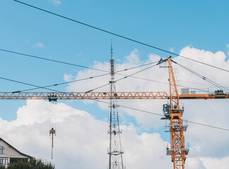 Yellow construction tower crane against blue sky.House under construction. Industrial skyline.