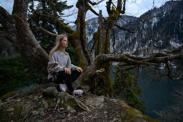 Fototapeta na wymiar Girl sits on a tree and meditates near lake Ritsa in Abkhazia