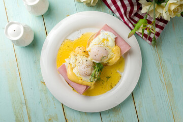 eggs Benedict with ham and classic sauce on white plate top view