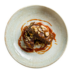 Brownie with caramel and nuts on brown plate isolated on white background top view