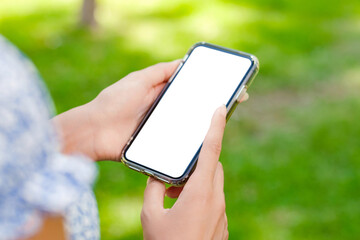 Young beautiful woman wearing summer dress on city park, outdoors hands holding phone touching finger mockup white blank display, mobile application tech concept, over shoulder closeup view.