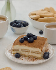 Dessert tiramisu decorated with blueberries .on the table coffee, a bowl of cookies and blueberries