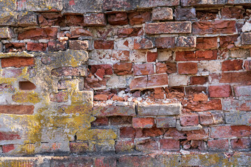Old brick wall with partially destroyed red brick. There are remnants of gray plaster and moss. Background. Texture.