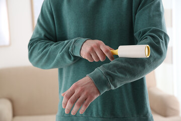 Man cleaning green sweatshirt with lint roller indoors, closeup