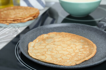 Delicious thin pancake in frying pan on induction stove, closeup