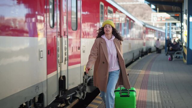 Happy young traveler woman with luggage boarding in the train at train station platform