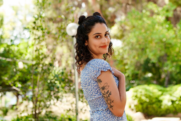 Side view of brunette woman wearing summer dress standing on city park, outdoors looking at camera while posing. Natural beauty concept. Beautiful girl. Pretty young woman.