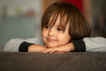 Obraz na płótnie Canvas Portrait of a three-year-old boy with long dark hair, at home. Cute smiling kid