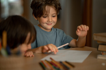 Two little boys, two brothers are sitting at home at the table and drawing with colored pencils. Child and creativity