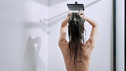 Back shot of a Caucasian female woman taking shower at home - obrazy, fototapety, plakaty