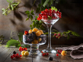 Red currants in a glass wine glass and raspberries and blackberries on a wooden table