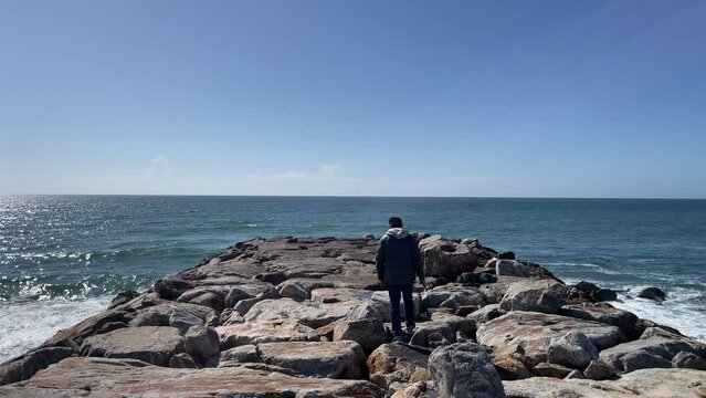 Man walking on rocks of breakwaters againt ocean.