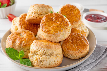 Homemade British Scones with cream cheese, strawberry jam and a cup of tea on a white wooden background.