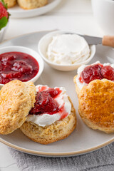 Homemade British Scones with cream cheese, strawberry jam and a cup of tea on a white wooden background.