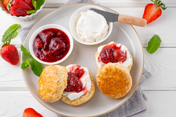 Homemade British Scones with cream cheese, strawberry jam and a cup of tea on a white wooden background.