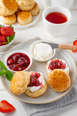 Homemade British Scones with cream cheese, strawberry jam and a cup of tea on a white wooden background.
