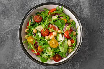 Salad with chickpeas, green leaves and fresh vegetables in a bowl on a gray concrete background. Healthy food. Top view, copy space.