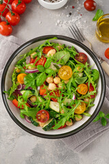 Salad with chickpeas, green leaves and fresh vegetables in a bowl on a gray concrete background. Healthy food. Top view, copy space.