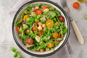 Salad with chickpeas, green leaves and fresh vegetables in a bowl on a gray concrete background. Healthy food. Top view, copy space.
