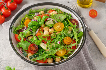 Salad with chickpeas, green leaves and fresh vegetables in a bowl on a gray concrete background. Healthy food. Top view, copy space.