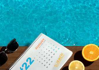 Top view of swimming pool with orange, lemon, sunglass and calendar on the wooden floor. Summer...