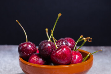 Cherries with drops in a bowl on a black background