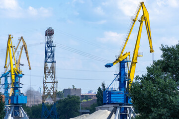 Fototapeta premium Big port cranes on the river. Extraction and transportation sand. Harbor crane loads water resources into the barge. Special equipment and water transport. River port. Industrial city.