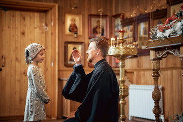 a priest blesses a little girl in a headscarf in an Orthodox church after a festive church mass