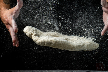 Hands throw up pizza dough and flour crumbles, dark background.