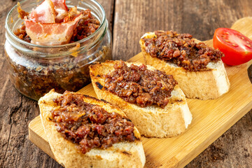 Homemade bacon jam on croutons and next to a jar of jam on an old wooden table.
