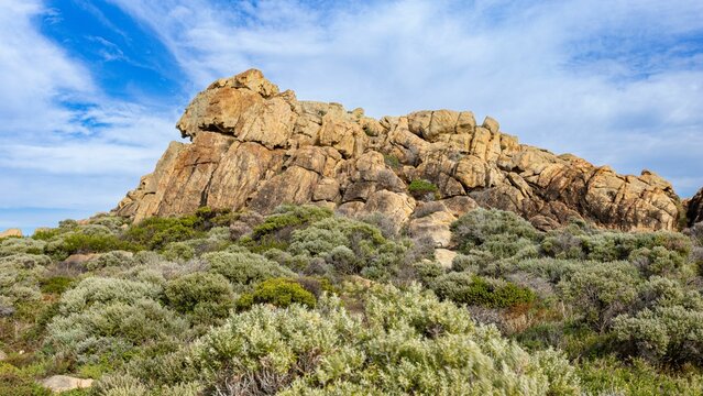 Scenic view of a rocky hill covered with green shrubs under a cloudy blue sky on a sunny day - Powered by Adobe